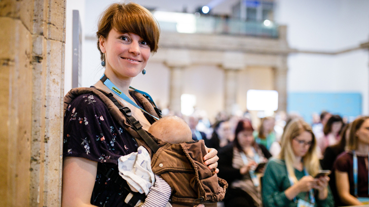 Eine Mutter steht mit Baby in einer Trage bei der Chefsache Konferenz 2019